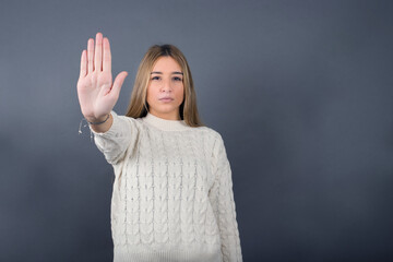 Beautiful young blonde woman wearing white sweater standing against gray background, 