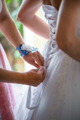 Bridesmaid with boutonniere on her hand, is helping bride to lace wedding white dress. Preparation element.	