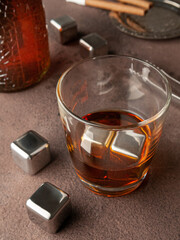 Steel cubes imitating ice. For cooling drinks. With a glass of whiskey. On a brown background. View...