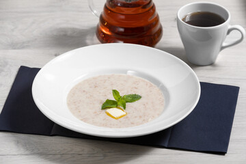 Milk porridge in a white plate with butter and mint leaves on a wooden background with a mug of tea. Healthy Breakfast, proper morning.