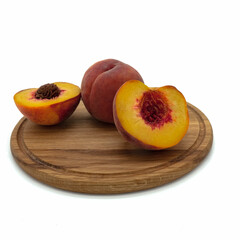 Pink peaches on a round wooden board. One ripe fruit is whole, the other is cut in half. Isolated over white background.