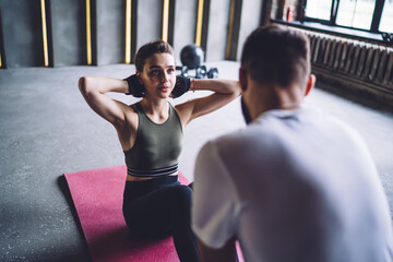 Naklejka premium Strong caucasian male and female couple in love having morning workout for keeping fitness goals and shape, teen 20s woman in activewear doing exercises with help of professional trainer in gym