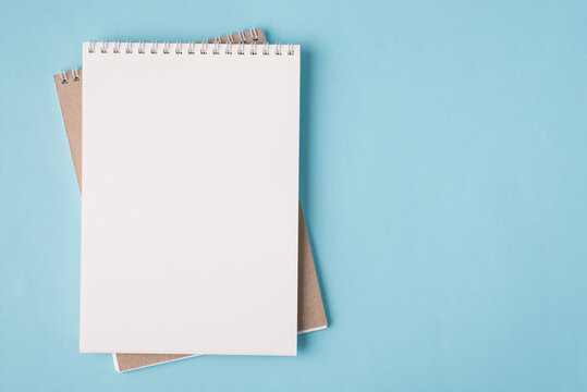 Top above overhead view flat lay photo of a blank notebook placed to the left side isolated on pastel blue color background with copyspace