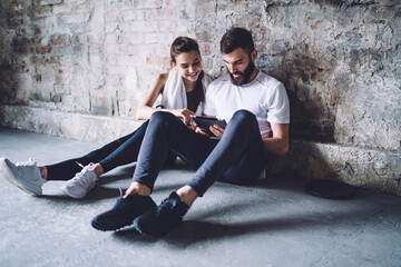 Smiling male and female couple in love checking news from social networks using tablet on break...