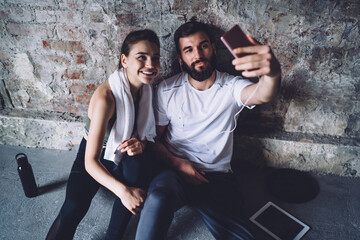 Positive young couple taking self portrait on smartphone after workout