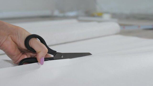 Close-up of a woman's hand cutting a sheet of Wallpaper with scissors for later pasting it on the wall.