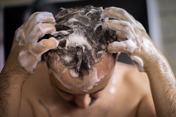 young bearded naked brunette man massaging his head in shower with shampoo foam or hair care product. Advertising for men's hair cosmetics or conditioner or antihairloss remedy