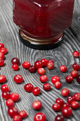 Cranberry jam in glass jars. Cranberries are scattered nearby. On wooden boards with a beautiful texture.