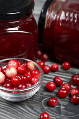 Cranberry jam in glass jars. Nearby berries are in a container and scattered over the surface. Close-up. On wooden boards with a beautiful texture.