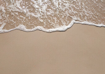 White foamy wave on the beach sand. Top view. Marine texture background