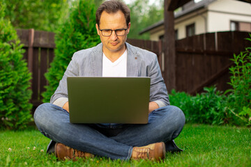 Middle aged businessman working on laptop outdoors, handsome man sitting on grass, sell...