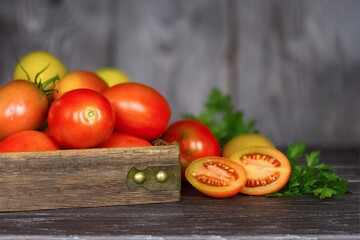 fresh red and yellow tomatoes in a wooden box close-up and sprigs of fresh parsley. background with the harvest of tomatoes and herbs.