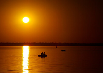 Naklejka premium Beautiful golden sunset over the lake with silhouettes of boats with people