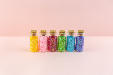 Small glass bottles with corks with multicolored shiny sequins asterisks stand in a row on a pink...