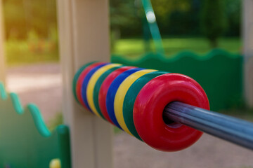 Detail of a children's playground in the park. Plastic abacus on a steel rod on a green background on a bright summer day