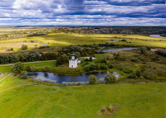 a panoramic view of the white old church on a green meadow between the tributaries of the river against the backdrop of thunderclouds filmed from a drone