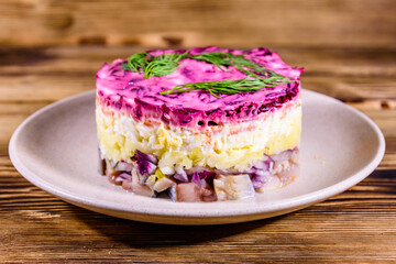 Ceramic plate with russian traditional new year salad herring under fur coat (shuba) and on rustic wooden table