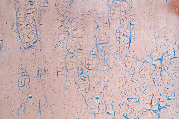 The surface of the old metal wall is pink. The paint layer has cracks of various shapes, the lower blue layer appears. Background. Texture.
