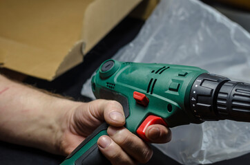 Male hands unpack and examine the electric drill.
