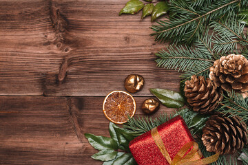 Christmas frame made of fir tree and magonia branches,golden cones,golden chestnuts and red gift box on the dark wooden rustic background.Christmas background.Copy space for text, top view.