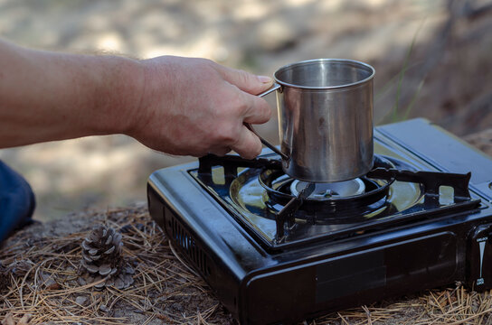 Herbal tea in a metal mug in hand over a portable gas stove