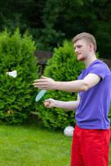 Young strong sport Caucasian man plays badminton with racquet and shuttlecock on green background. concept of amateur game of badminton on meadow, outdoor activities.
