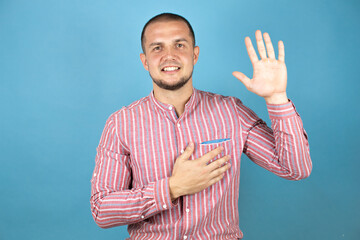 Russian business man over blue background smiling swearing with hand on chest and fingers up,...