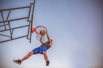 Young man does a slam dunk playing outdoor basketball. - obrazy, fototapety, plakaty