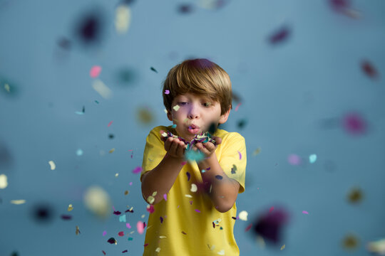 beautiful child blowing confetti on colored blue background.