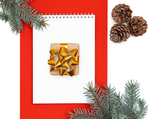 White notepad for notes on a red background with gift at the center, cones of a Christmas tree and branches of a Christmas tree.