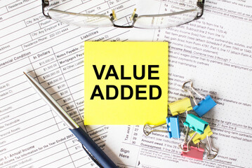 Yellow sticker with text Value Added. Next to it is a blue pen with colored stationery clips and...