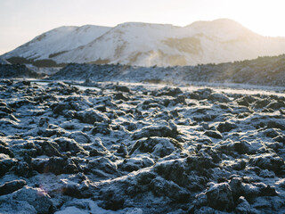 Snow covered lava field in winter near the Blue Lagoon, Reykjanes Iceland. Steam rising from the Lagoon in background, backlit by late afternoon sun.