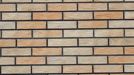 a fragment of flat new brickwork in the structure of a wall or fence with blocks of different light shades of brown and contrasting dark cement joints
