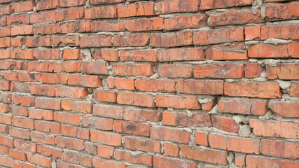 an aging crumbling red brick wall of a building or fence with a rough texture of old broken bricks and gray drips of dry cement between blocks
