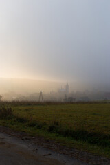 Mystery way. Misty landscape with fog, trees, fields, village and road.  