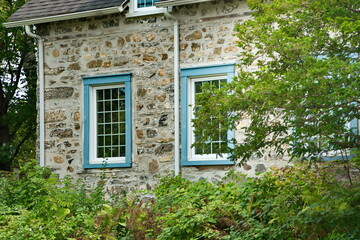 Fototapeta na wymiar The stone wall of a house framed by green trees and foliage.