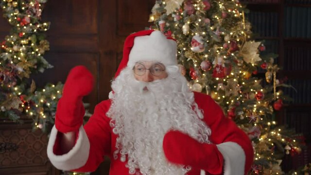Portrait of joyful Santa Claus dancing in decorated house moving arms in gloves having fun indoors. Celebrations, lifestyle and holidays concept.