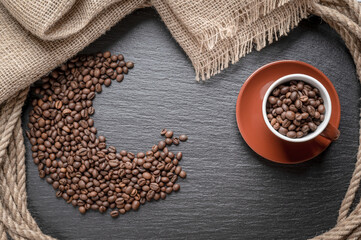 Coffee background, top view with copy space. Brown coffee cup with beans inside. Coffee beans on a dark stone background. 