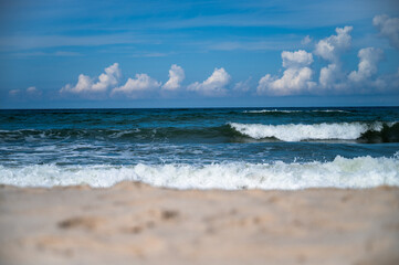 Stormy surf on the seashore, with white foam on the yellow sand. Skyline over the sea with blue sky and cumulus clouds