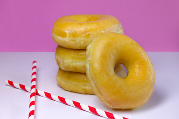 Four Donuts or Classic Donuts Stack with Two Red Stripe Straw on a White and Pink Background.