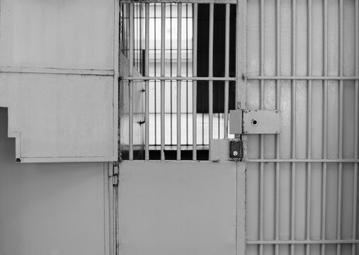 Monochrome shot of the prison or jail cell door made of steel metal bars with the old lock and peeling paint. Imprisonment concept