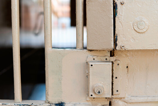 A closeup of the lock of a jail cell. Old-fashion worn-out prison lock with beige peeling paint on the jail cell door. Prison interior.