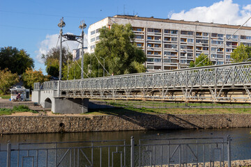 Naklejka premium View on pedestrian bridge in Ivanovo with metal posts, fence and light lamps under blue sky, river, city buildings
