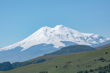 Fototapeta premium Scenic view of the highest peak in Europe, mount Elbrus with green hills on a Sunny summer day.