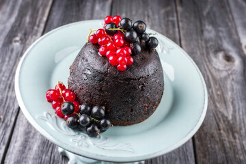 Traditional Australian plum pudding fresh forest berries offered as close-up on a design plate on a wooden table