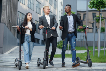 Confident happy multiracial office colleagues discussing business project go near office building with electric scooters © gorynvd