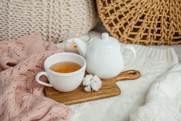 A mug of hot tea, a teapot, a wooden stand on an ottoman. Cozy autumn. Winter breakfast. Cotton.