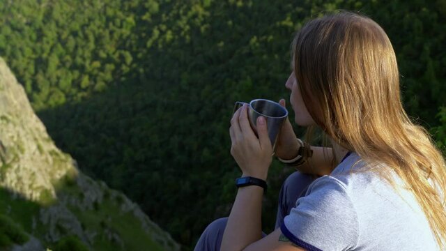 A woman is drinking tea on a background of mountains. Close-up.
