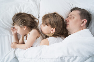 Obraz na płótnie Canvas Kids, dad sleep together in bed on pillows under blanket. Family joint sleeping. Father with cute little daughters. Insomnia, night bedtime.Sweet dreams. arly wake up,rise to kindergarten,school,work