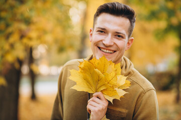 Portrait of handsome guy smiling and holding a bouquet of autumn leaves in the park